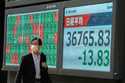 A person walks in front of an electronic stock board showing Japan's Nikkei index at a securities f…